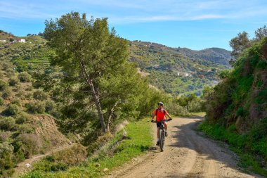 İspanya 'nın Endülüs kenti Nerja yakınlarındaki Frigiliana beyaz köyünde elektrikli dağ bisikletiyle bisiklet süren hoş bir son sınıf öğrencisi.