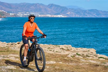 İspanya, Endülüs, Nerja yakınlarındaki Costa Blanca sahil şeridinde son sınıf öğrencisi güzel bir bayan elektrikli dağ bisikletiyle bisiklet sürüyor.