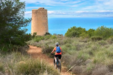 İspanya, Endülüs, Nerja yakınlarındaki Costa Blanca sahil şeridinde son sınıf öğrencisi güzel bir bayan elektrikli dağ bisikletiyle bisiklet sürüyor.