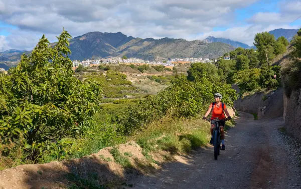 İspanya 'nın Endülüs kenti Nerja yakınlarındaki Frigiliana beyaz köyünde elektrikli dağ bisikletiyle bisiklet süren hoş bir son sınıf öğrencisi.