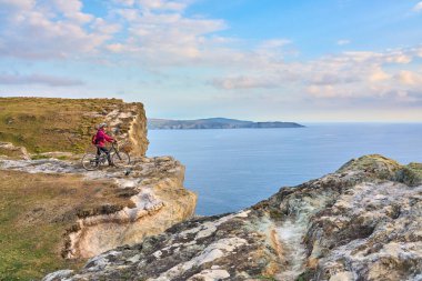 İrlanda Cumhuriyeti 'nin güneybatısındaki Sheeps Head, County Cork' un kayalıklarında gün batımında bisiklet süren son sınıf öğrencisi hoş bir kadın.