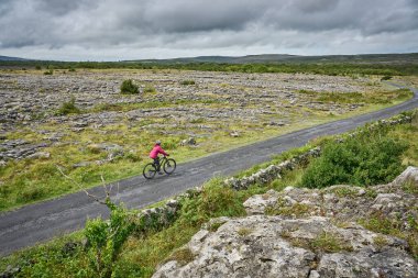 İrlanda Cumhuriyeti 'nin batı kesiminde Ballyvaughan, County Clare yakınlarındaki Burren' in engebeli karst bölgesinde bisiklete binen son sınıf öğrencisi hoş bir kadın.