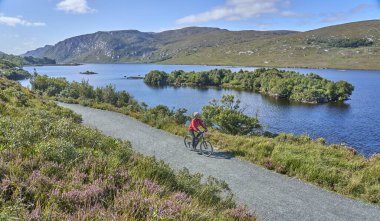 nice senior woman on mountain bike, cycling at Lough Beagh in the Glenveagh National park, near Churchill, Donegal, northern Republic of Ireland clipart