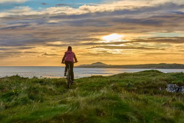 İrlanda Cumhuriyeti 'nin batı kesimindeki Sillerna, Grallagh, County Galway' in altın kumsalında gün batımında bisiklet süren son sınıf öğrencisi hoş bir kadın.