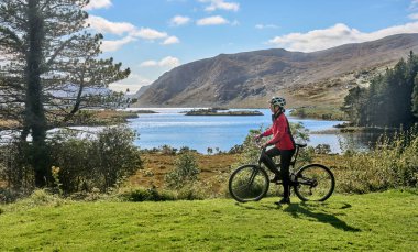 nice senior woman on mountain bike, cycling at Lough Beagh in the Glenveagh National park, near Churchill, Donegal, northern Republic of Ireland clipart