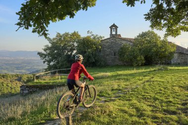 nice senior woman riding her electric mountain bike between olive and cypress trees in the hills near Arezzo in Tuscany,Italy