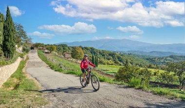nice senior woman riding her electric mountain bike between olive and cypress trees in the hills near Arezzo in Tuscany,Italy