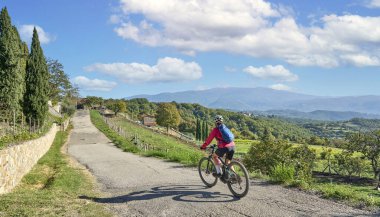 nice senior woman riding her electric mountain bike between olive and cypress trees in the hills near Arezzo in Tuscany,Italy