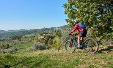 nice senior woman riding her electric mountain bike between olive and cypress trees in the hills near Arezzo in Tuscany,Italy