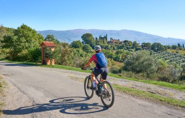 nice senior woman riding her electric mountain bike between olive and cypress trees in the hills near Arezzo in Tuscany,Italy