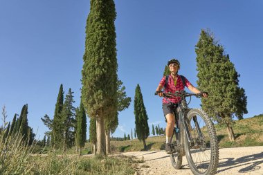 nice senior woman riding her electric mountain bike between olive and cypress trees in the hills near Arezzo in Tuscany,Italy