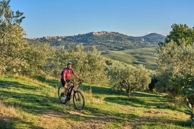 nice senior woman riding her electric mountain bike between olive and cypress trees in the hills near Arezzo in Tuscany,Italy