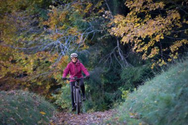 sympathetic active senior woman, riding her electric mountainbike in the colorful autumn forests of the Bavarian Alps near Oberstaufen, Germany