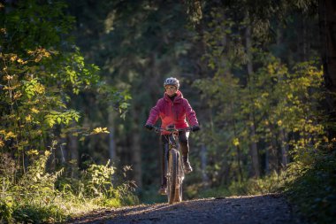 sympathetic active senior woman, riding her electric mountainbike in the colorful autumn forests of the Bavarian Alps near Oberstaufen, Germany
