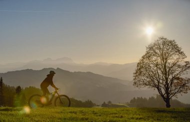 Aktif bir kadın gün batımında elektrikli dağ bisikletini sürüyor Saentis Dağı 'nın muhteşem siluetinin önünde, Appenzell Switthe
