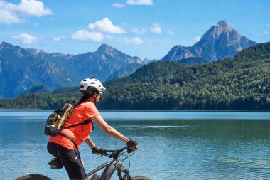 Fuessen, Doğu Allgau, Bavyera, Almanya yakınlarındaki Weissensee Gölü 'nde elektrikli dağ bisikleti süren güzel yaşlı kadın.