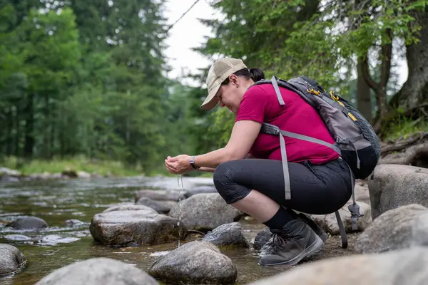a woman on a hike stops by a stream and draws water summer time