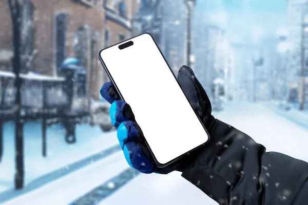 Using a mobile phone on the street while it is snowing. Isolated display for app promotion. Man's hand holding a phone with a winter glove