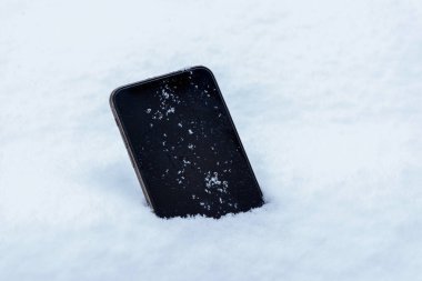 Lost mobile phone in the snow concept. Close-up. Blank device display with snowflakes on it