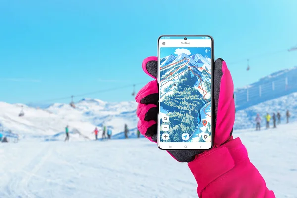 Ski map on smart phone in woman hand with pink glove. Ski and snowboard app concept for route and distance tracking concept. Skiers and ski slopes in the background