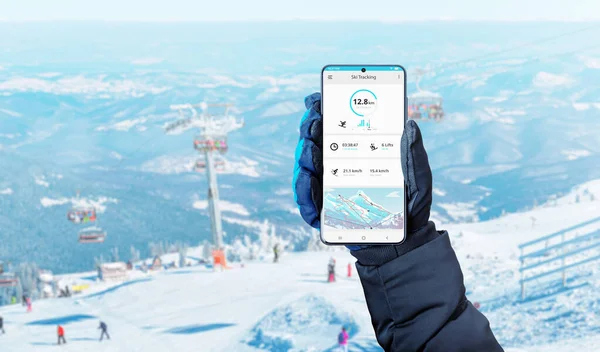 Smart phone in hand with glove and ski tracking app on phone display. Ski slopes in background concept