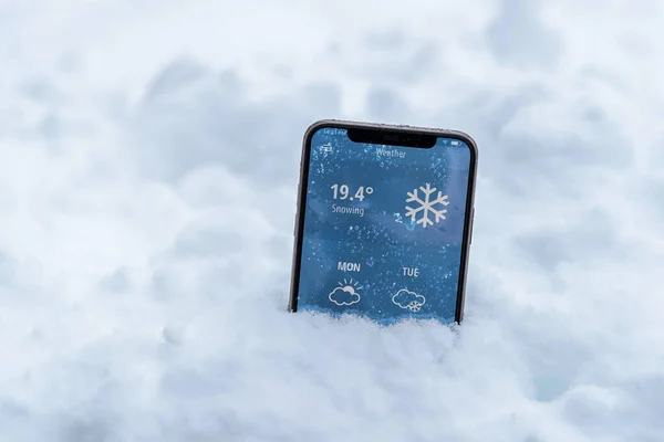 Phone in the snow with a weather forecast shows the temperature in fahrenheit