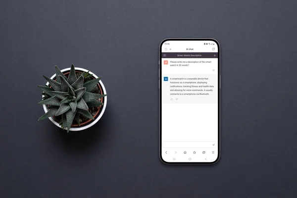Mobile phone on the desk with a chatbot AI app. Conceptual design of app to communicate with artificial inteligence. Plant beside, top view, flat lay