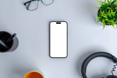 Modern çalışma ortamı, boş bir telefon ekranı ile model alınarak, bir kulaklık, bitki, bardak, kalem ve bir kahve kupası gibi ofis gereksinimleri arasında yer alıyor. Üst görünüm, düz konum
