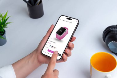 Akıllı telefonla online akıllı saat alışverişi. Kapalı bir masada elinde modern bir akıllı telefon tutan bir insan. Etrafı bir fincan kalem, bir saksı ve kahve bardağıyla çevrili.