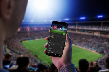 Futbol maçındaki adam olasılıkları ve skoru takip ediyor. Online spor bahisleri konsepti. Futbol stadyumu ve arka planda kalabalık