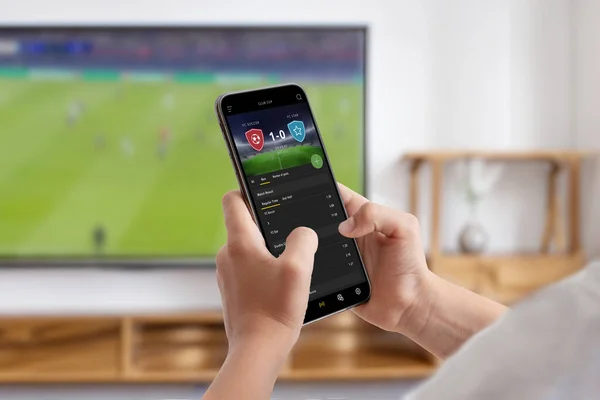 Man watches a soccer match on TV and follows online betting on his phone