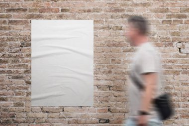Kırışık, beyaz A3 posteri, tuğla duvara yapışmış. Yanında bir adam yürüyor. Reklam veya pazarlama kampanyası tasarım tanıtımı