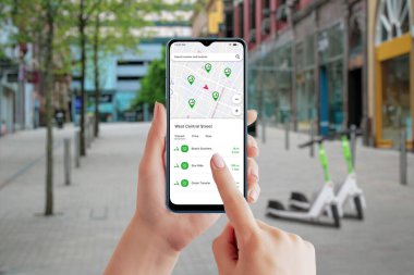 Akıllı telefondan elektrikli scooter paylaşım uygulaması. Şehir sokağı ve arka planda scooterlar