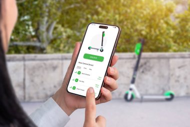 Uygulamalı, cep telefonlu bir elektrikli scooter kiralamak. Arka plandaki uygulama tarafından kilitlenmemiş scooter