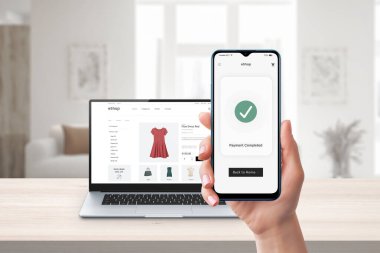 Telefon çevrimiçi ödeme. Arka planda dizüstü bilgisayar ve e-ticaret sitesi var. Çevrimiçi alışveriş ve güvenli elektronik ödemeler için dijital işlem ekranı