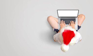 Kırmızı Noel şapkalı çocuk dizüstü bilgisayarda çalışıyor. İzole edilmiş bir ekranı var. Zeminde şenlik verimliliği. Boşluğu kopyala
