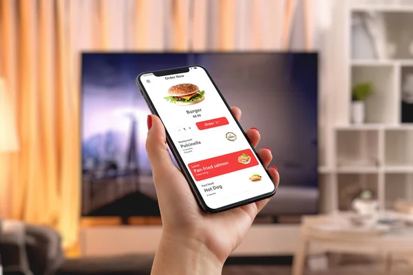 Man orders a burger via smartphone in the living room, creating a perfect blend of tech convenience and enjoyment in fast food in front of the TV