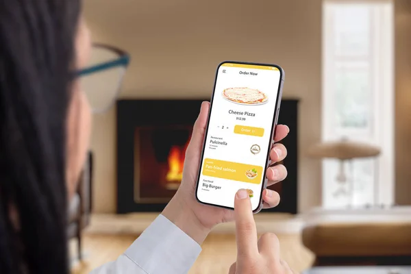 Woman ordering pizza online with a smartphone app in a cozy room by the fireplace. Seamless convenience for a delightful dining experience at home