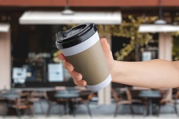 Logo mockup on a paper takeaway cup held in hand in front of a coffee shop