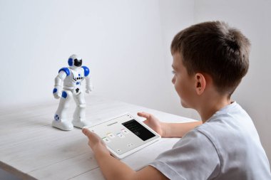 Çocuk, elinde tabletle masadaki robotun çalışmasını programlıyor.