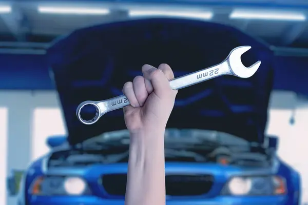 Wrench in hand in front of a blue car with an open engine compartment. Ready for service and maintenance. Professional automotive concept