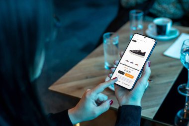 Kadın ayakkabı almak için cep telefonu kullanıyor. Kullanıcı dostu arayüzü olan modern ekommerce uygulaması. Kullanım ve verimlilik için çevrimiçi alışveriş kavramı