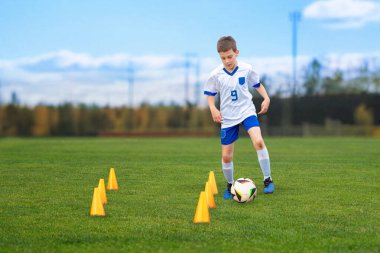 Genç çocuk bir eğitim merkezinde koni etrafında manevra yaparak futbol çalışıyor. Spor, gençlik, spor ve beceri geliştirme içeriği için mükemmel