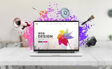 Laptop on a desk displaying a web design concept page featuring a colorful water splash, surrounded by creative tools like a brush, megaphone, wrench, camera, scissors, and gear clipart