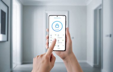 Güvenlik uygulaması arayüzü olan akıllı bir telefonu tutan kapı kilidi, güvenlik kamerası ve alarm gibi güvenlik özelliklerini kontrol eden bir el. Modern güvenlik kavramı, uzaktan izleme