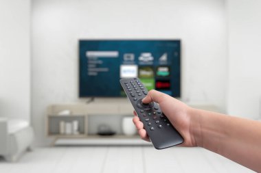 Hand holding a remote control for a smart TV, featuring app buttons for streaming services. Concept of versatile entertainment, showcasing the functionality of smart TVs for various viewing purposes and apps