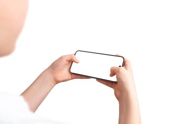 Çocuk akıllı telefonu oyun pozisyonunda tutuyor, ekrandaki iki başparmağını da kullanıyor. Omuz üstü görünüm, izole ekran ve arkaplan, oyun tanıtımı için mükemmel