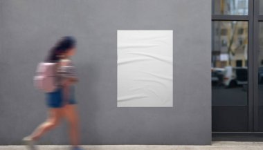 Bina girişinin yanında beyaz poster modeli. Çantalı kız geçiyor, modern promosyon posterlerini sergilemek için mükemmel.