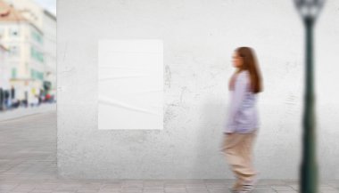 Bina duvarında beyaz poster tasarımı olan bir sokak sahnesi. Kız hareketli yürüyor, dinamik reklam gösterisi için ideal.
