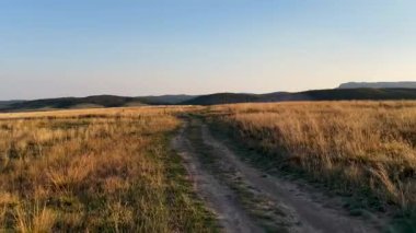 Kırsal toprak yol kuru çayırlarda kıvrılır, kırsal yaşamın basit ritimlerini yankılar.